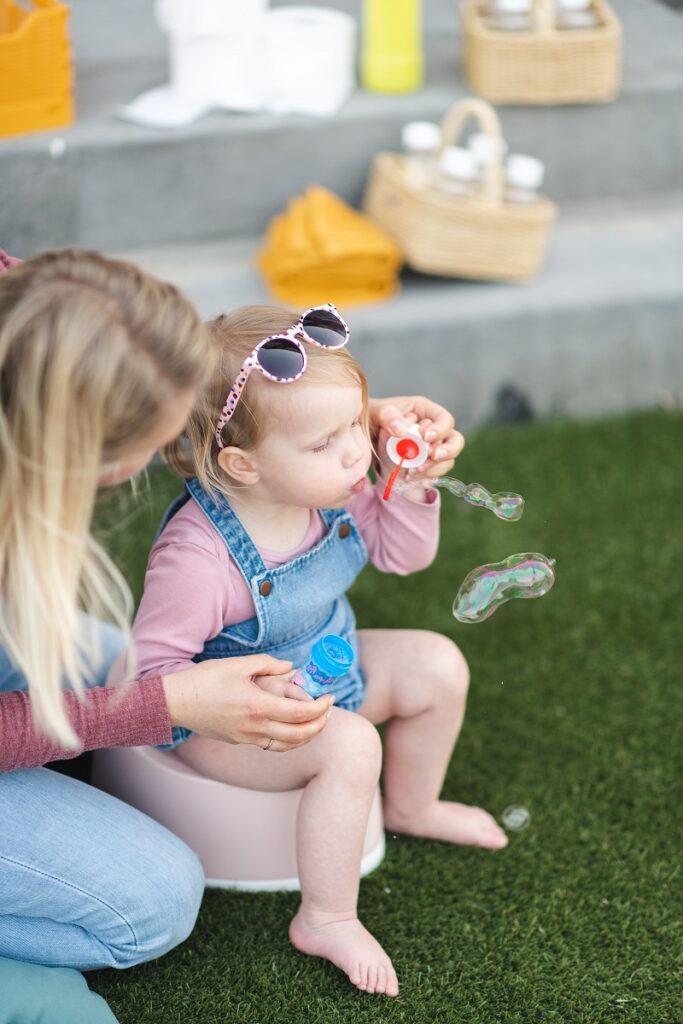 An image of a little girl sitting on a potty with her mother sitting beside her, blowing bubbles in the air. The girl looks happy and interested, as she watches the bubbles floating around her. Succesful potty training tips by best potty training app have helped the child to be potty trained. This is helpful when child won't sit on potty