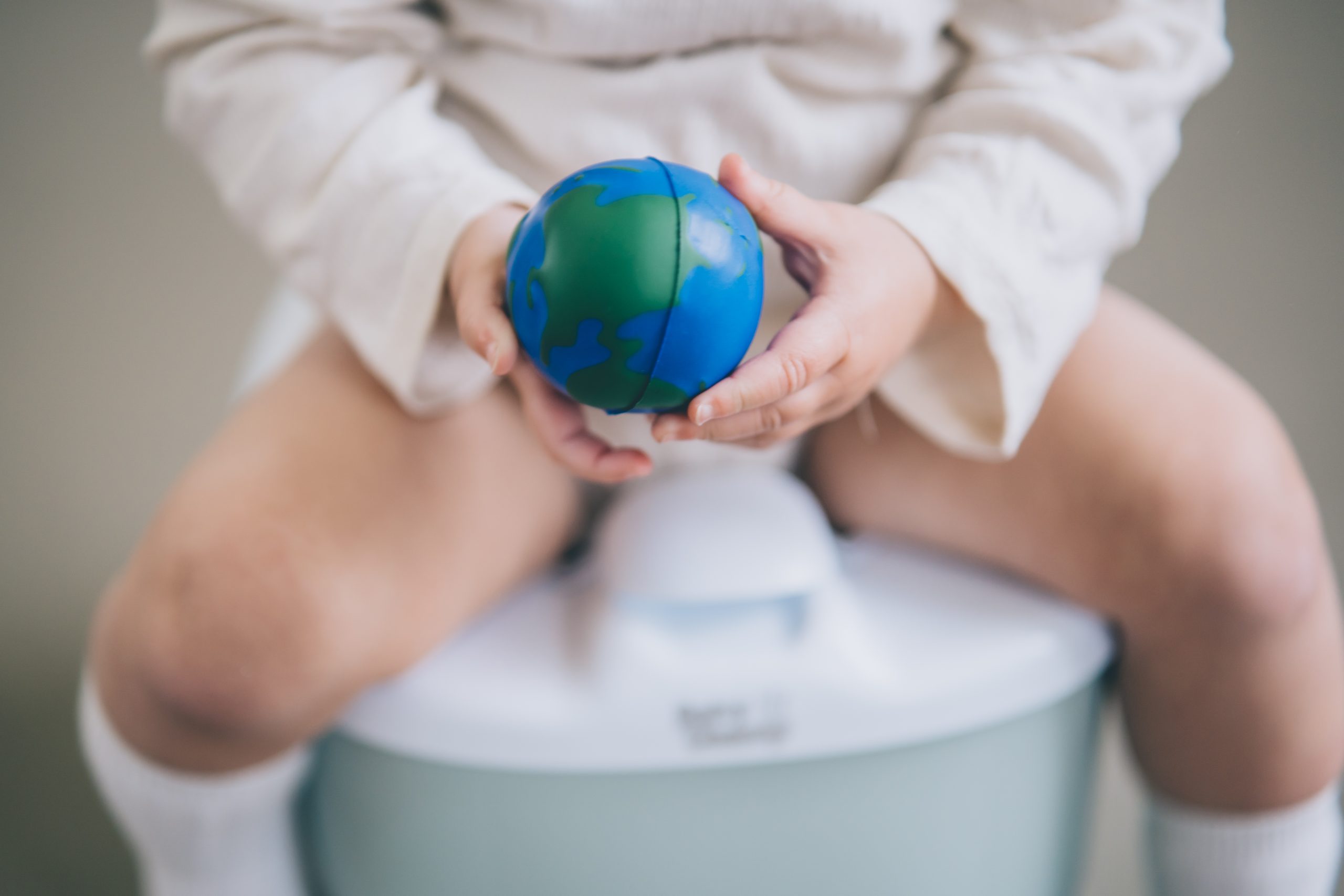 green toilet habits A young child sitting on a white plastic potty with their pants pulled down. The child is holding an earth globe in their lap, looking at it with interest.