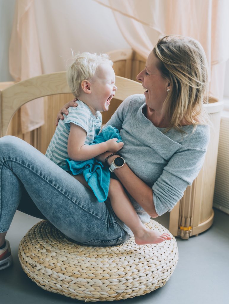 A mother and child sitting, both laughing and smiling while looking at each other during potty training. The child is holding a towel napkin, while the mother has her arm around the child's back. They are happy to choose the right potty training method