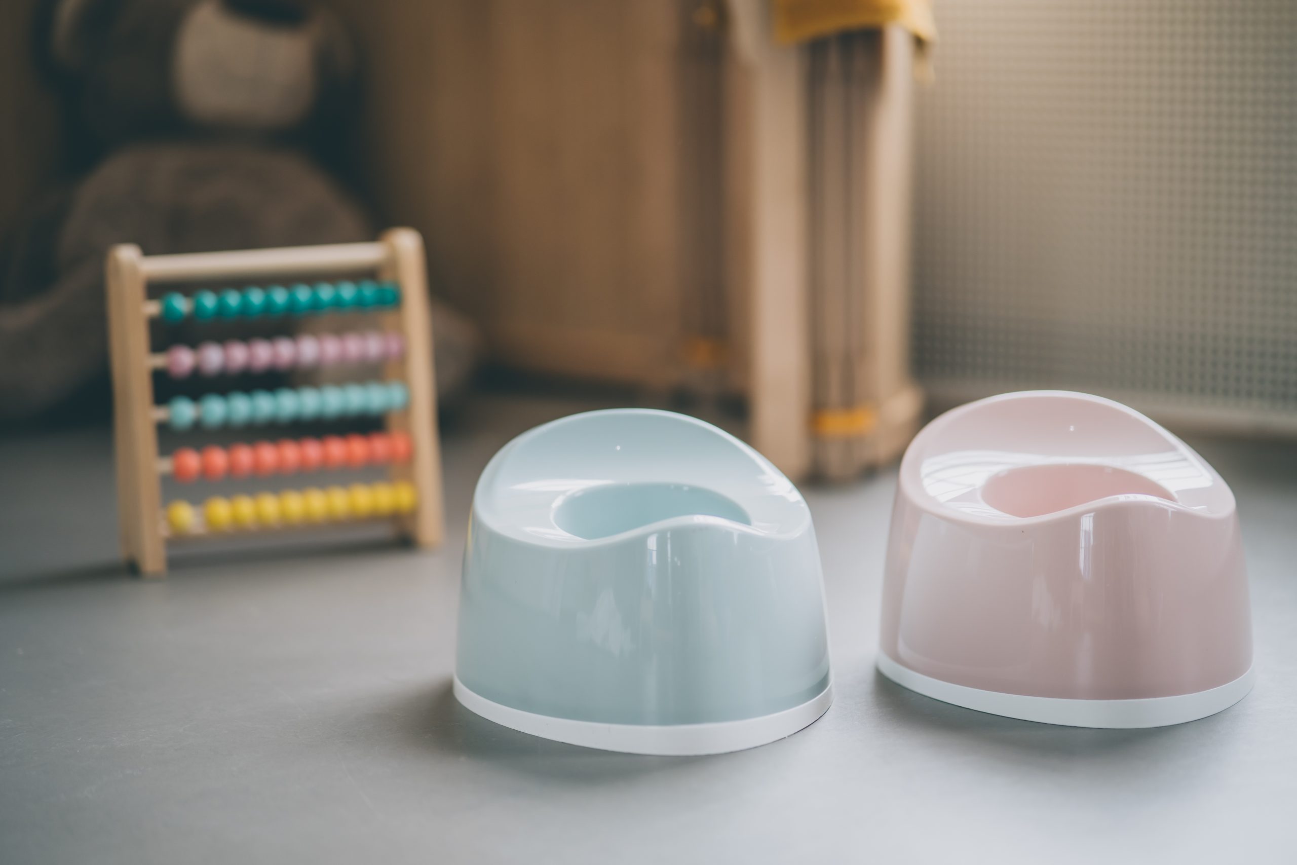 Choosing Right Potty Training Methods: Foxx and Azrin’s and Brazelton’s Potty Training Methods Two potty seats side by side, one in blue and one in pink, with toys visible in the background. These potty seats are used for potty training/toilet training toddlers in which children can poop, pee, wee, or poo.