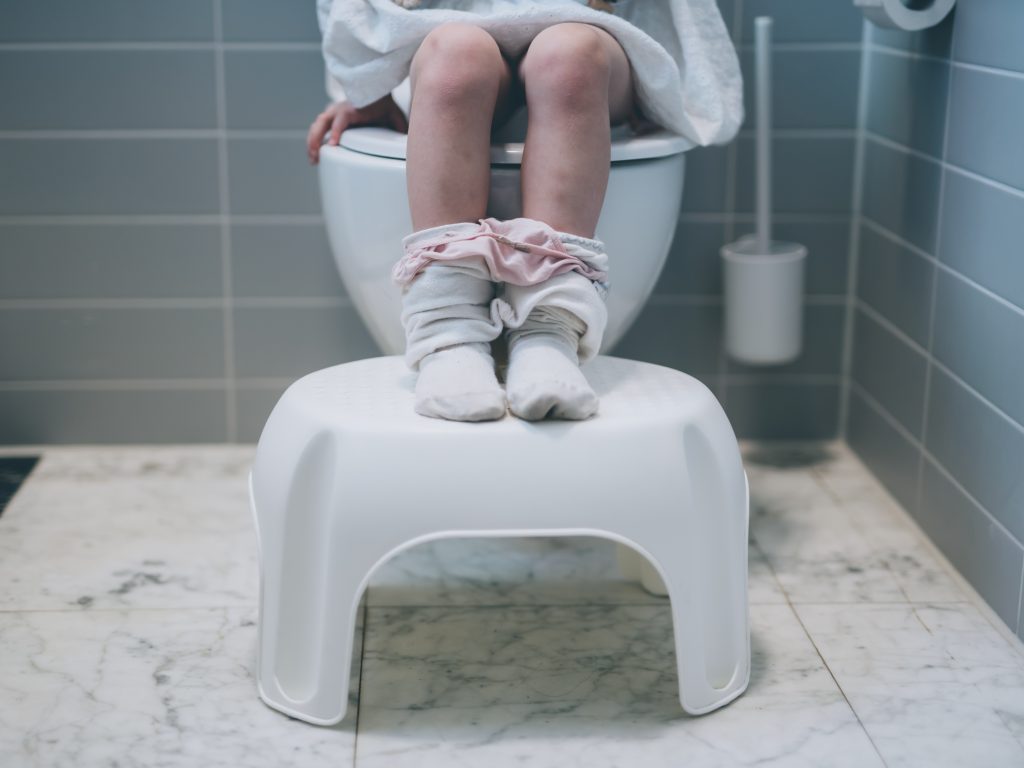 A child sitting on potty chair or toilet seat with pants down during potty training / toilet training. The child is suffering from constipation or poo problems.