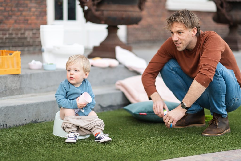 Potty Training And Traveling: 6 Tips and Tricks Child on potty holding cup, father / dad sitting close to boy. looking away. being outside. blog traveling with potty training