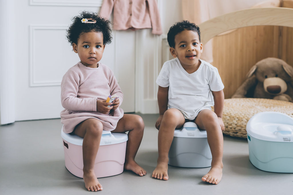 a boy and a girl sitting on a pink and blue potty, ready for potty training twins