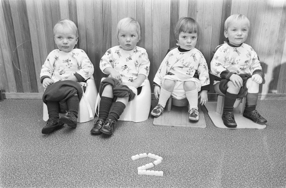 Black and white picture of 4 children potty training by sitting in a row on potties in 1977. When to start potty training.