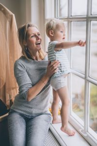 little boy standing by the window in pants together with his mother sitting by the window, both looking outside and smiling. blog for traveling with toddler potty training